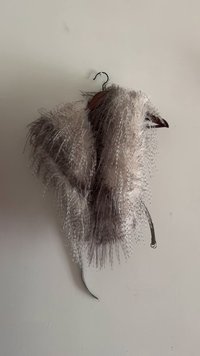 Feathered bolero jacket in cream and grey hues, featuring a textured design with long, flowing strands and a clasp for secure closure.