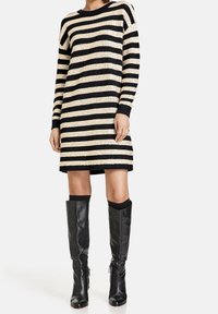 Zwart en beige gestreepte gebreide jurk met een ronde hals en lange mouwen, gecombineerd met hoge zwarte leren laarzen. De jurk heeft ribgebreide manchetten.