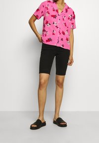 Camicetta rosa a maniche corte con motivo floreale, abbinata a pantaloni corti in denim neri e sandali neri a scivolo. Tessuto morbido con una vestibilità comoda.