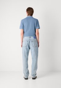Camisa de polo de algodón azul claro combinada con jeans de mezclilla azul claro, con un corte relajado y etiqueta HUGO en la parte trasera de la cintura.