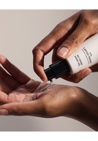 Gel pour les mains sans rinçage dans une bouteille blanche avec une pompe noire ; liquide distribué dans une paume. Texture lisse, design minimaliste et étiquette épurée.