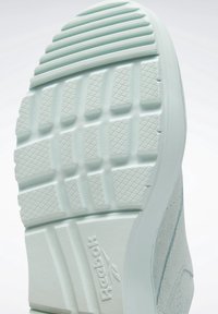 Jasnoniebieska podeszwa sportowego buta z teksturowanymi wzorami gripu i małym, wypukłym logo. Posiada gładki, zakrzywiony kształt z wyglądem wyściełanym.