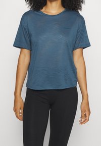 Niebieska koszulka z krótkim rękawem, wykonana z lekkiej, teksturowanej tkaniny w falisty wzór. Posiada okrągły dekolt i subtelne logo na lewej piersi.