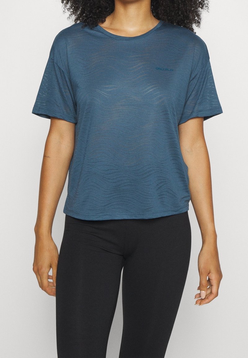 Niebieska koszulka z krótkim rękawem, wykonana z lekkiej, teksturowanej tkaniny w falisty wzór. Posiada okrągły dekolt i subtelne logo na lewej piersi.