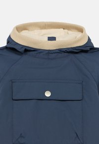 Σκούρο μπλε μπουφάν με μπεζ ριμπ γύρο γιακά, που διαθέτει μία μπροστινή τσέπη με καπάκι και ασημένιο κουμπί τύπου κούμπωμα. Ομαλό, ελαφρύ ύφασμα.