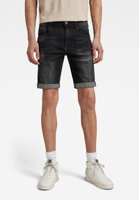 Black denim shorts with rolled cuffs, featuring front and back pockets. Paired with light-colored high-top sneakers and white socks.