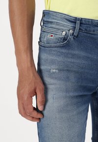Blugi din denim albastru cu o croială slim, ușor uzată și un patch cu logo vizibil pe buzunarul din spate. Design clasic cu cinci buzunare.