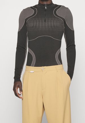 Černý přiléhavý top s dlouhými rukávy, polovičním zipem a kontrastními světle geometrickými vzory. Kombinován s béžovými kalhotami s vysokým pasem.