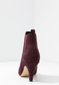 Stivaletto in suede bordeaux con tacco a stiletto sottile, caratterizzato da un design elegante e un'etichetta sul retro per una facile indossabilità.
