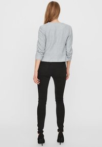 Světle šedá zkrácená bunda s tříčtvrtinovými rukávy, texturovaná látka, v kombinaci s černými skinny džíny a černými podpatky.