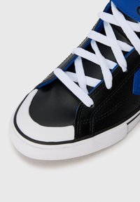 Svart högsko-sneaker med vit gummisula, blå accenter och vita snörningar. Slät lädermaterial med rund tå och texturerad yta.