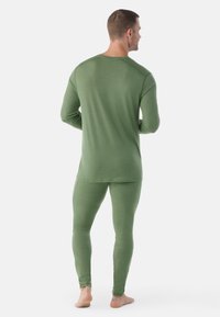 Grünes langärmeliges Oberteil und enganliegende Leggings aus glattem Stoff. Es hat einen runden Halsausschnitt und gerippte Akzente an den Schultern.