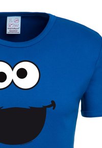 Blue cotton t-shirt featuring a large black face design with white eyes and a smiling mouth. Round neck and short sleeves.