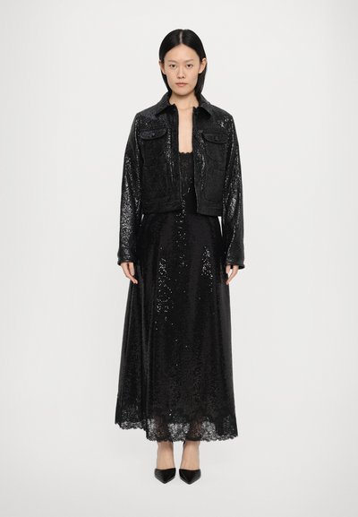 Crna haljina sa sequins detaljima i čipkastim rubovima, u kombinaciji s kratkim crnim teksturiranim sakoom s prednjim džepovima. Ovaj look upotpunjuju crne cipele na visoku petu.