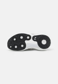 Sort og hvid sportsko sål med en struktureret gummioverflade, der har cirkulære mønstre og et Under Armour-logo i midten.