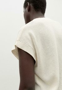Short-sleeve, textured knit top in light beige, featuring rolled cuffs and a loose fit. Back view highlights the fabric's open weave.