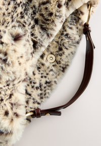 Sac en fausse fourrure à motif tacheté beige et marron, doté d'une bandoulière en cuir marron et d'une fermeture à bouton en métal doré. Texture douce.