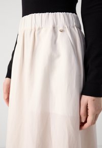 Donna che indossa una maglietta nera a maniche lunghe e una gonna bianca a vita alta con cintura elastica e un piccolo bottone metallico decorativo.