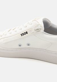 Baskets en cuir blanc à la finition lisse, dotées d'une fermeture éclair sur le côté, d'une semelle texturée et du nom de la marque "BOSS" en noir.