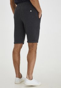 Shorts gris foncé en tissu doux et texturé, avec une taille élastique, des poignets repliés et une poche arrière unique. Portés avec des baskets blanches.
