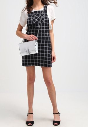 Czarna i biała sukienka w kratę z regulowanymi ramiączkami, zestawiona z srebrną torebką crossbody. Model nosi czarne sandały na obcasie.