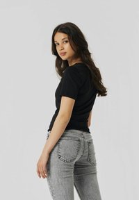 Zwarte aangesloten T-shirt gecombineerd met grijze high-waisted jeans. T-shirt heeft korte mouwen; de jeans hebben een vervaagde textuur en achterzakken.