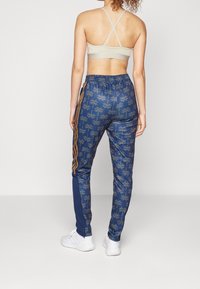 Mörkblå joggare med palmträdsmönster, elastisk midja, guld sidostråk och en slim fit. Bärs med en ljus beige sport-BH.