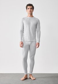 Grå långärmad tröja och åtsittande leggings i lättviktsmaterial, med en jämn textur och subtil branding på bröstet.