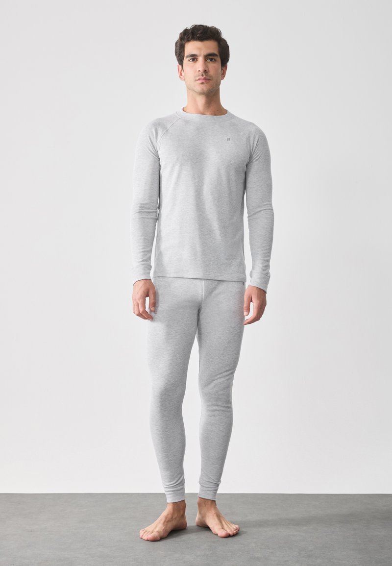 Grå långärmad tröja och åtsittande leggings i lättviktsmaterial, med en jämn textur och subtil branding på bröstet.