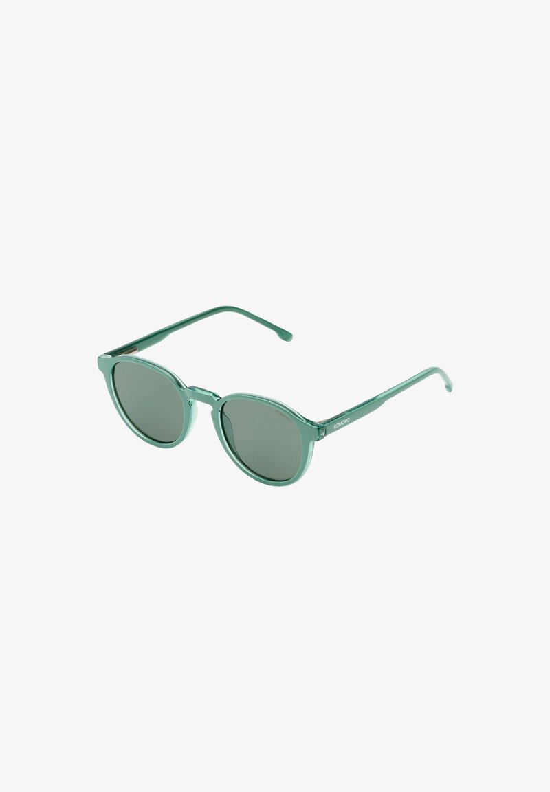 Lunettes de soleil à monture ronde en plastique vert, avec des verres teintés foncés, un design légèrement translucide et des branches fines inclinées vers l'extérieur.