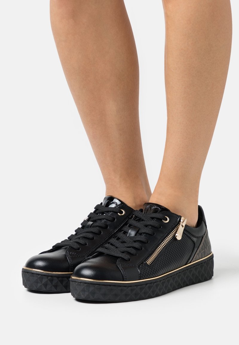 Black sneakers with textured patent leather and mesh design, featuring gold zipper accents and a diamond-patterned black sole.