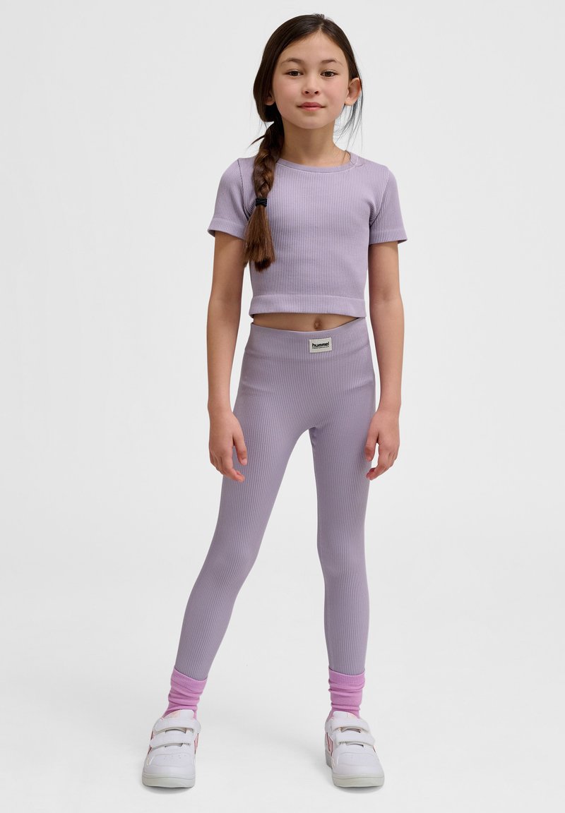 Lila ribbad crop top och leggings-set, med en figurnära design, mjukt material och logomärke; matchad med vita sneakers och rosa strumpor.