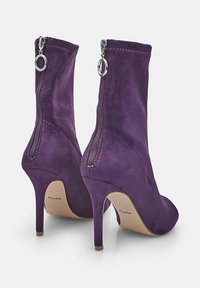 Violet nubuck-korkokenkät, joissa on takana vetoketjut ja pyöreät vetimet, sekä beige pohjat, näkyvät takakulmasta.
