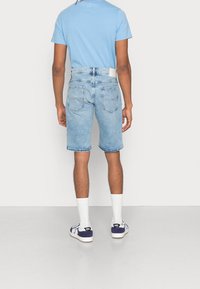 Vaaleansininen t-paita yhdistettynä vaaleisiin farkkushortseihin. Shortseissa on suora leikkaus, takataskut ja hieman kulunut helma. Valkoiset sukat ja tummansiniset kengät.