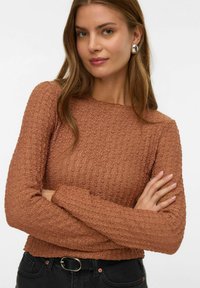 Rdzawy longsleeve z teksturowanej tkaniny, w prążki, z okrągłym dekoltem, zestawiony z czarnymi spodniami z wysokim stanem i paskiem.