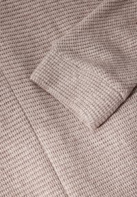 Tessuto beige chiaro con texture e un leggero motivo a nido d'ape. Una manica piegata è visibile, che mostra un materiale morbido e a maglia.