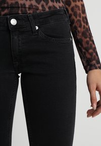 Czarne dżinsy z dopasowanym krojem, z zapięciem na guzik, kieszeniami z przodu i widocznymi przeszyciami. Gładka tekstura.