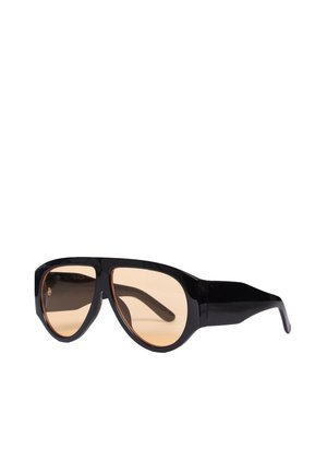 Occhiali da sole con montatura nera, grandi lenti rotonde color marrone chiaro e aste spesse e curve, mostrati su sfondo bianco.