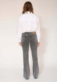 Jean gris évasé à taille haute avec des poches à l'arrière, associé à une chemise blanche à manches longues. La chemise présente des poignets boutonnés et un design simple.