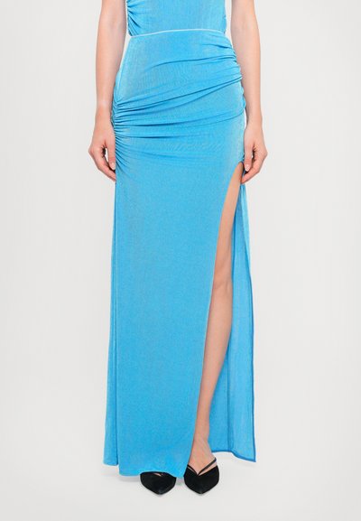 Blauwe jurk maxi met geplooide textuur, voorzien van een hoge split en flatterende drape, gecombineerd met zwarte punten schoenen.