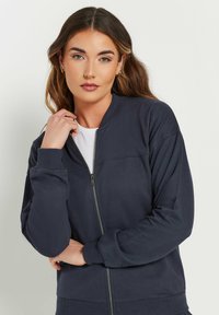 Marineblauwe zip-up sweatshirt van zacht stof met ribgebreide boorden en tailleband, met een eenvoudig ontwerp en een rits aan de voorkant.
