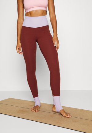 Leggins bordeaux avec une taille haute lilas et des accents aux chevilles. Le tissu est lisse et extensible, idéal pour le sport.