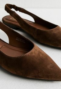 Bruine suède slingback flats met een spitse neus, een elastische hielband en een gladde bruine binnenzool. Minimalistisch ontwerp en een laag profiel zool.