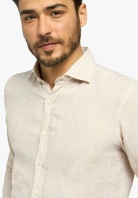 Camicia di lino beige con colletto, cinque bottoni e superficie texture. Presenta un design slim fit e una leggera lucentezza.