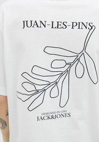 Hvid bomulds T-shirt med en sort kontur af et blad design på ryggen, med teksten "JUAN-LES-PINS" og "DESIGNED IN CPH JACK&JONES".