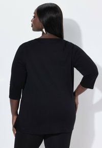 Zwarte lange mouw tuniek met een losse pasvorm, ronde halslijn, met een zijsplit en een gladde, zachte stoftextuur. Te combineren met leggings.