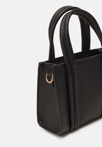 Musta tekonahkainen käsilaukku, jossa on kaksi pyöreää kahvaa, jämäkkä muoto, kultaiset yksityiskohdat ja ommellut korostukset sivuilla.