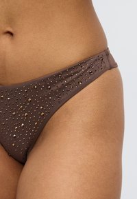 Καφέ κάτω μέρος μπικίνι με λείο ύφασμα και διάσπαρτες διακοσμητικές χάντρες, τονίζοντας έναν κομψό, μινιμαλιστικό σχεδιασμό.