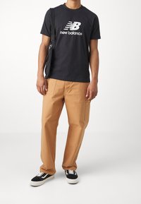 Czarna bawełniana koszulka z białym logo "New Balance", zestawiona z beżowymi spodniami cargo z kieszeniami. Czarno-białe sneakersy dopełniają stylizację.
