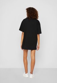 Zwarte oversized t-shirt jurk met korte mouwen, van zachte katoen, met een rechte snit, gecombineerd met witte sneakers.